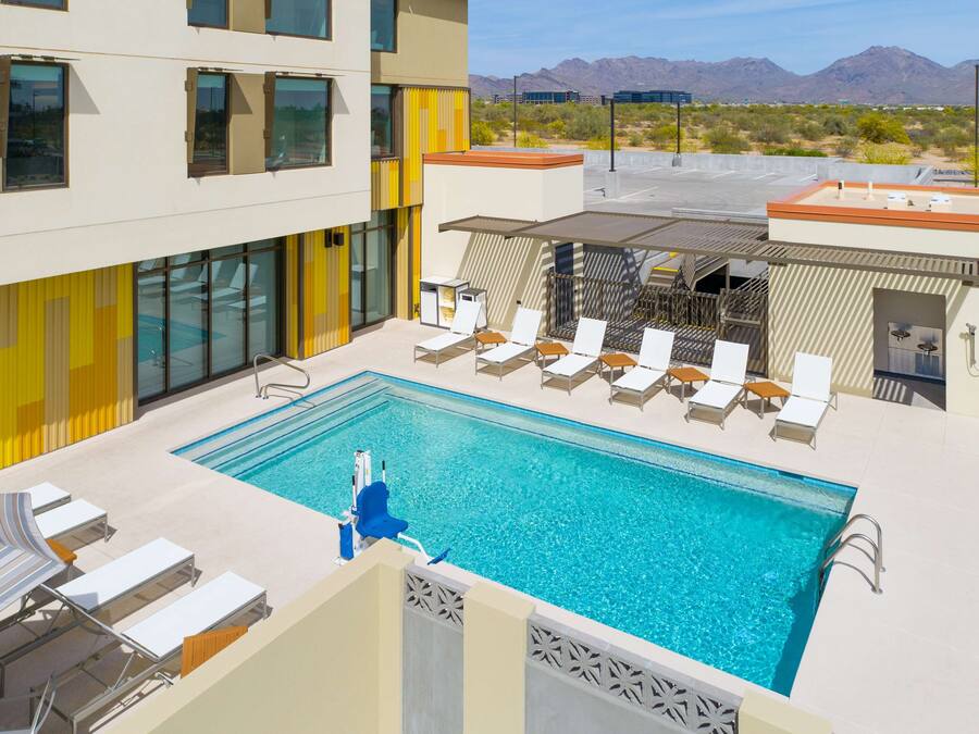 A rooftop pool with lounge chairs, a covered seating area, and a view of mountains.