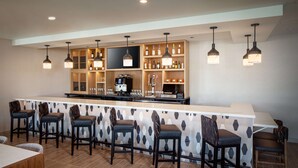A bar area with a long counter, multiple stools, and overhead pendant lighting. - Hyatt House North Scottsdale (Scottsdale)