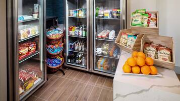 A refrigerated display case with various food items and beverages, a basket of snacks, and a wooden crate with packaged goods.