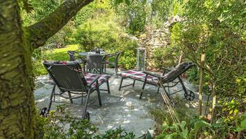 Un patio exterior con una mesa y sillas, rodeado de abundante vegetación y un muro de piedra.