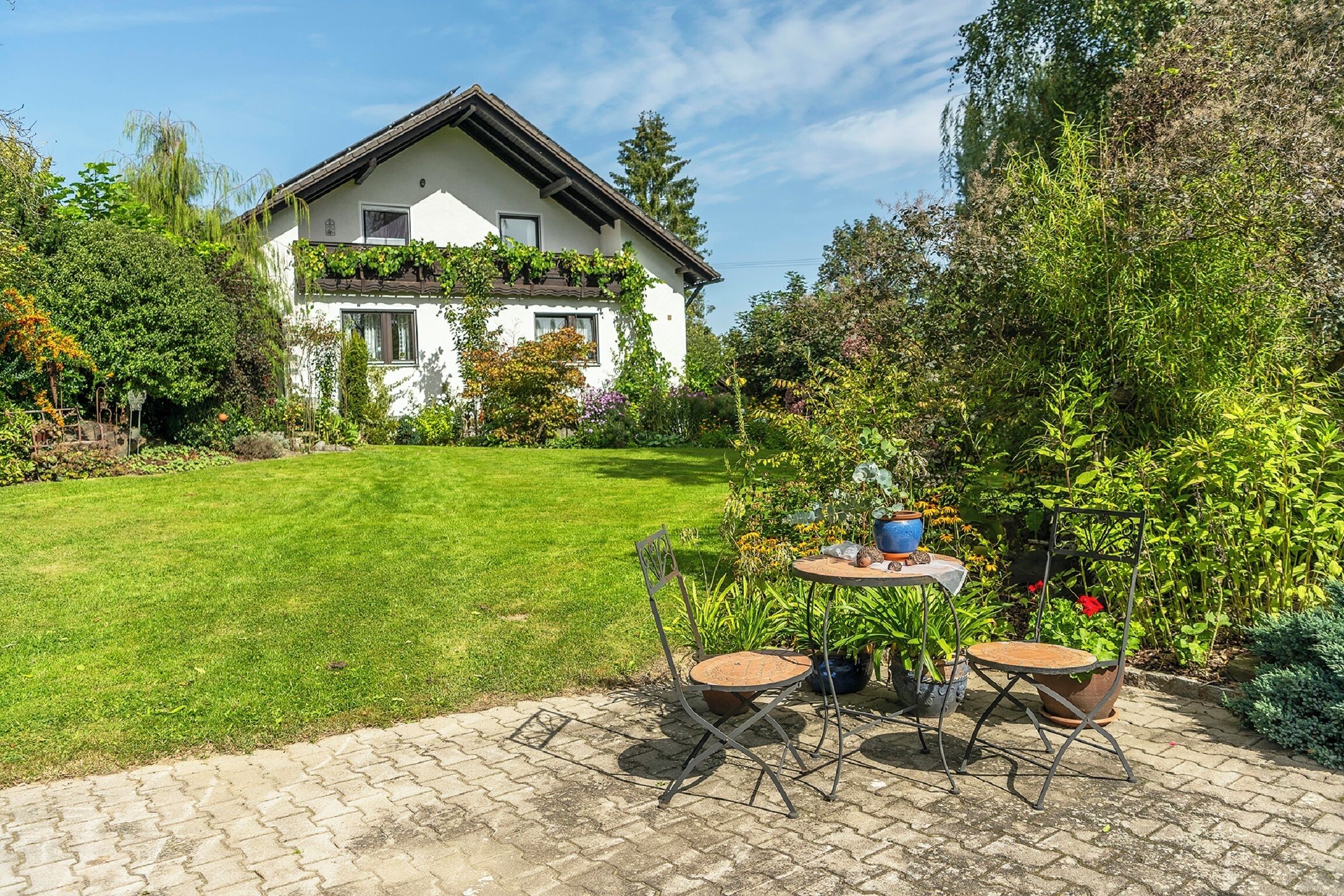 Et hus med have, fliseterrasse og et bord med stole.