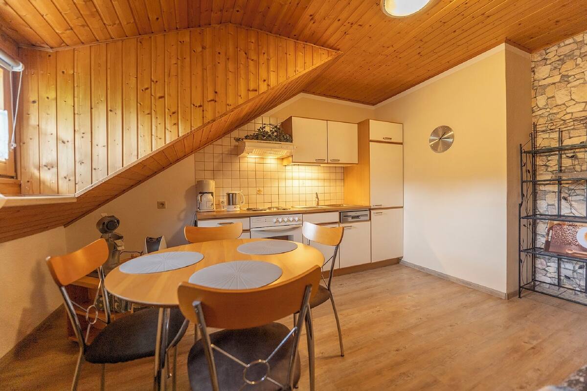 A kitchen with wooden ceiling, a dining table with chairs, and a stone wall with a shelf.