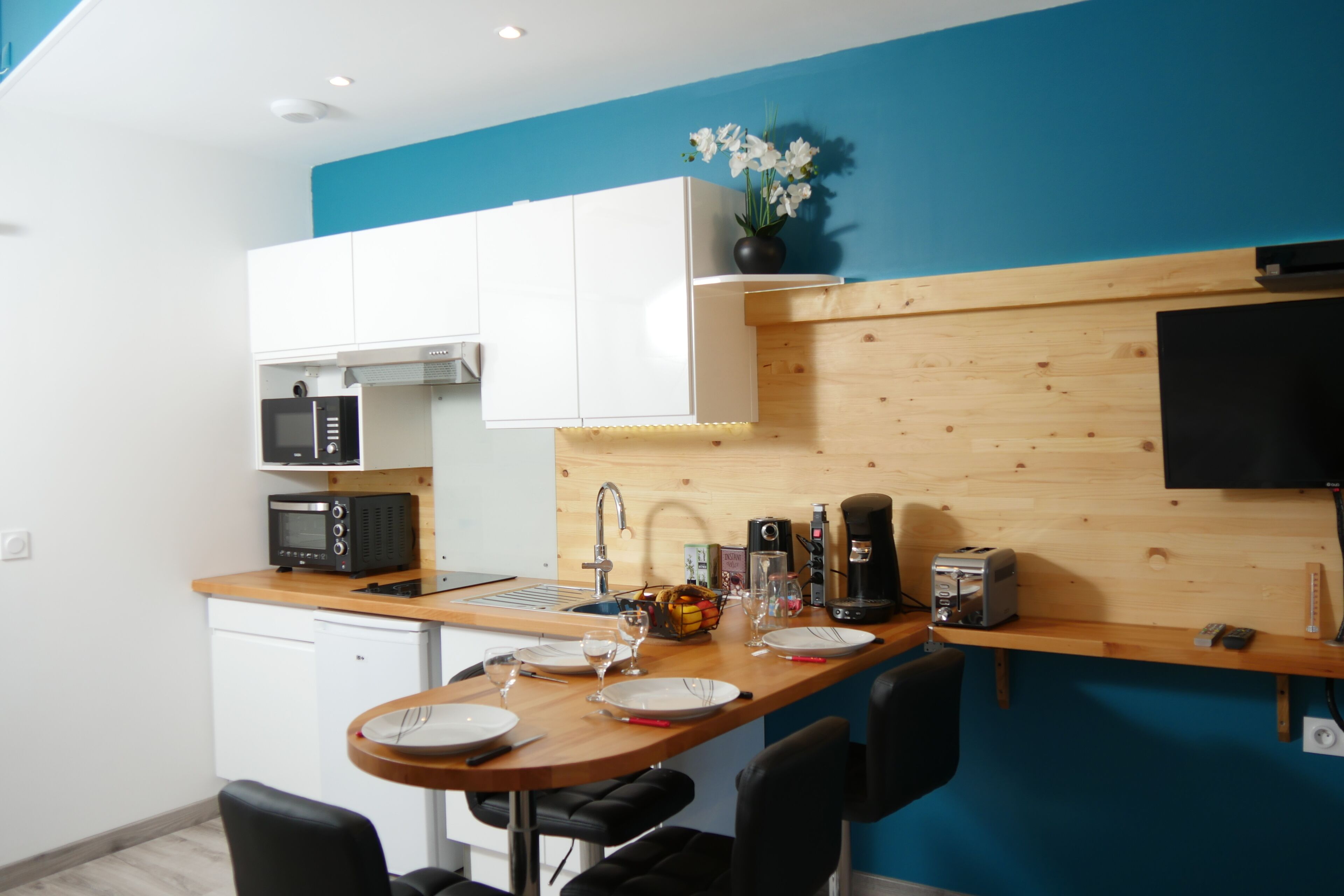 A compact kitchen with white cabinets, a wooden countertop, a microwave, a toaster, and a sink.