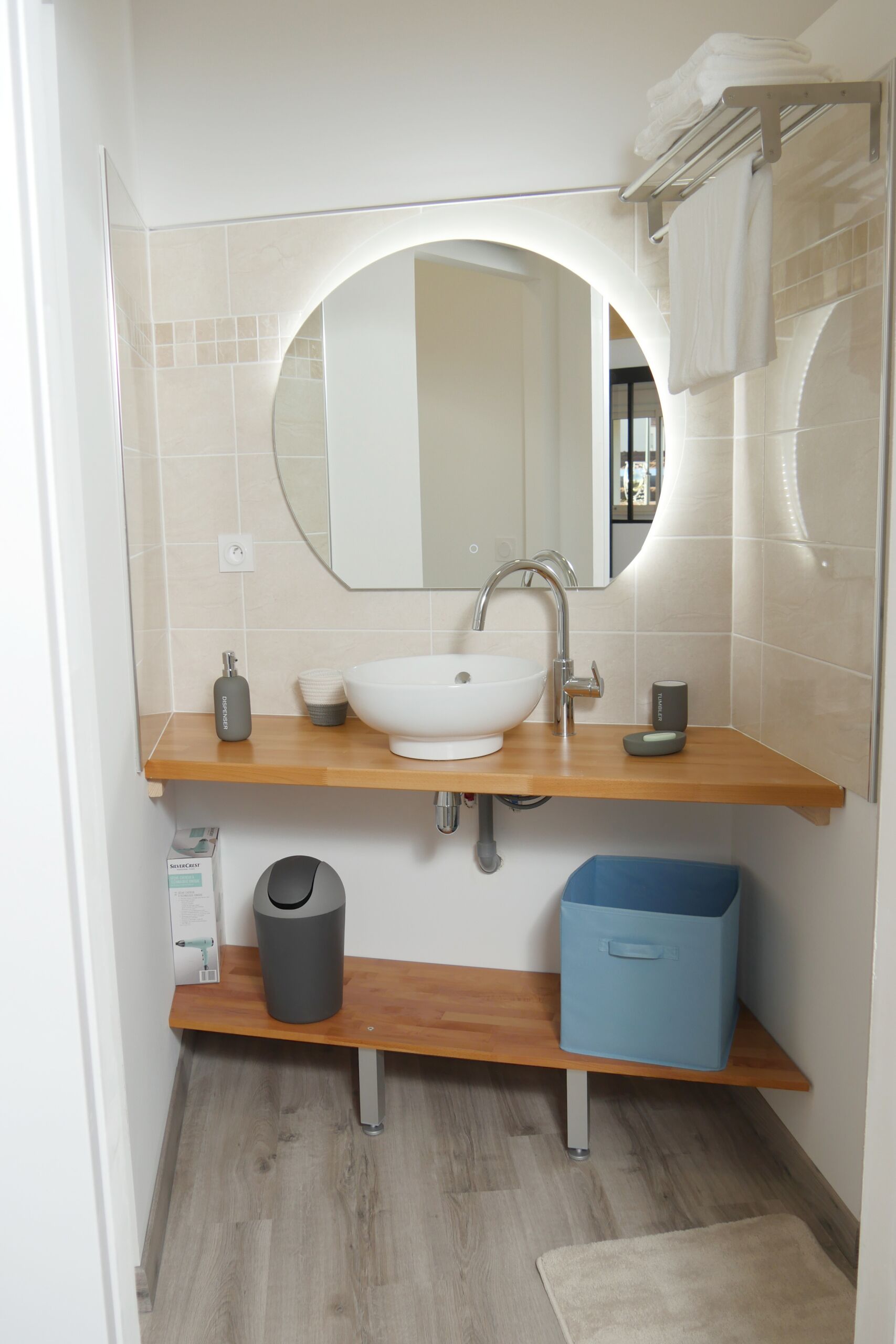 Un baño moderno con un lavamanos blanco, un espejo y un cesto azul para guardar objetos.