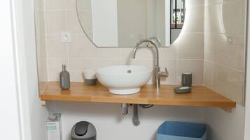 Un baño moderno con un lavamanos blanco, un espejo y un cesto azul para guardar objetos.