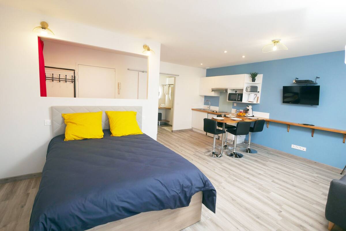 A modern bedroom with a large bed, a desk, and a kitchenette.