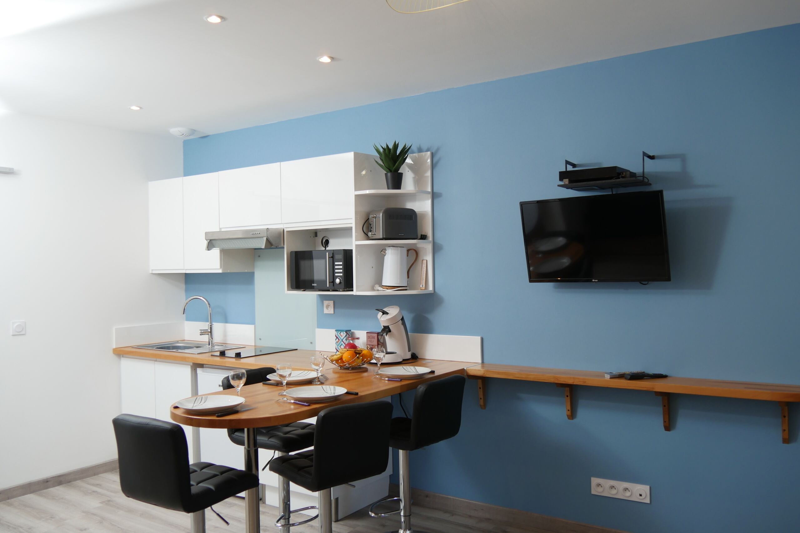 Una cocina moderna con armarios blancos, encimera de madera y televisión empotrada.