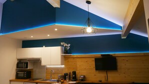 A modern kitchen with wooden beams, a built-in microwave, a sink, and a flat-screen TV mounted on the wall. - Appart Hôtel Albi (Albi)