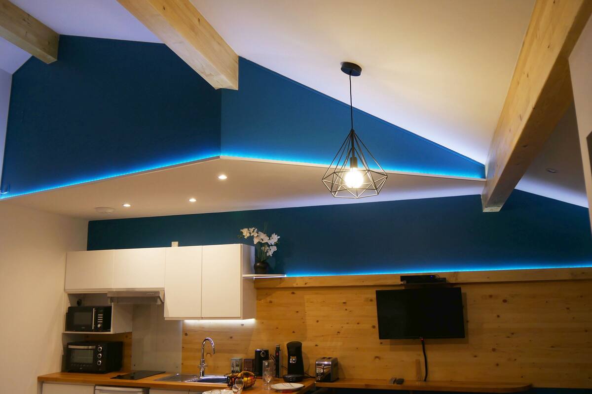 A modern kitchen with wooden beams, a built-in microwave, a sink, and a flat-screen TV mounted on the wall.