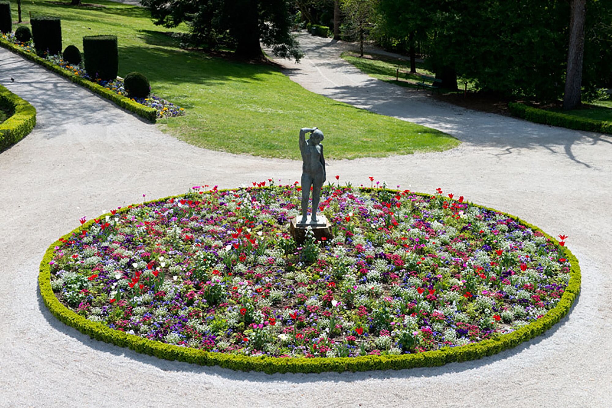 Un parterre circulaire agrémenté d’une statue au centre, entouré d’une variété de fleurs aux couleurs vives.
