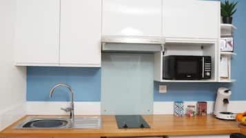 A compact kitchen with white cabinets, a stainless steel sink, a microwave, a coffee maker, and a small plant on the counter.