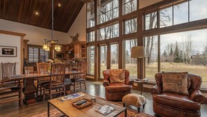 A spacious living room with a large window, a dining area with wooden furniture, and a cozy seating area with leather chairs. - Arnica Cabin at Jackson Hole Golf and Tennis (Jackson)