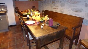 Un comedor rústico con una mesa de madera preparada para dos personas, rodeada de sillas. Hay una vela y una botella de vino sobre la mesa, y dos lámparas colgantes arriba.