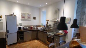 Una cocina moderna con refrigerador, estufa y lavamanos. Hay armarios de madera, una encimera y una mesa de comedor con sillas.