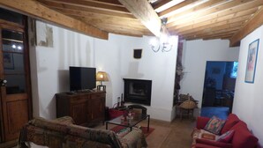 Una sala de estar con sofá, un sillón rojo, televisión, chimenea y techo de madera.