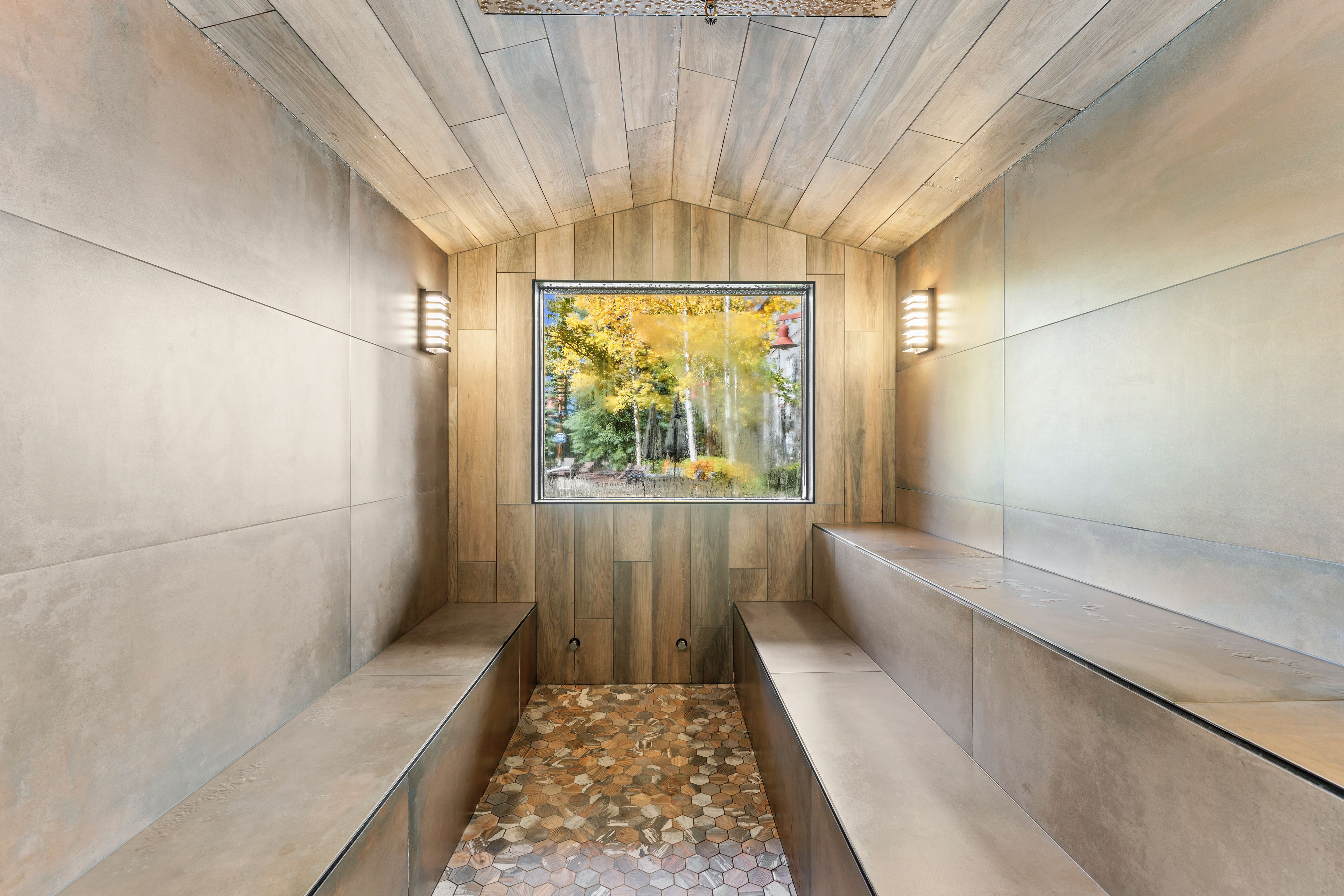 Ein modernes Interieur mit Holzbalkendecke, einer Glaswand mit Blick auf Bäume und einem gemusterten Boden.