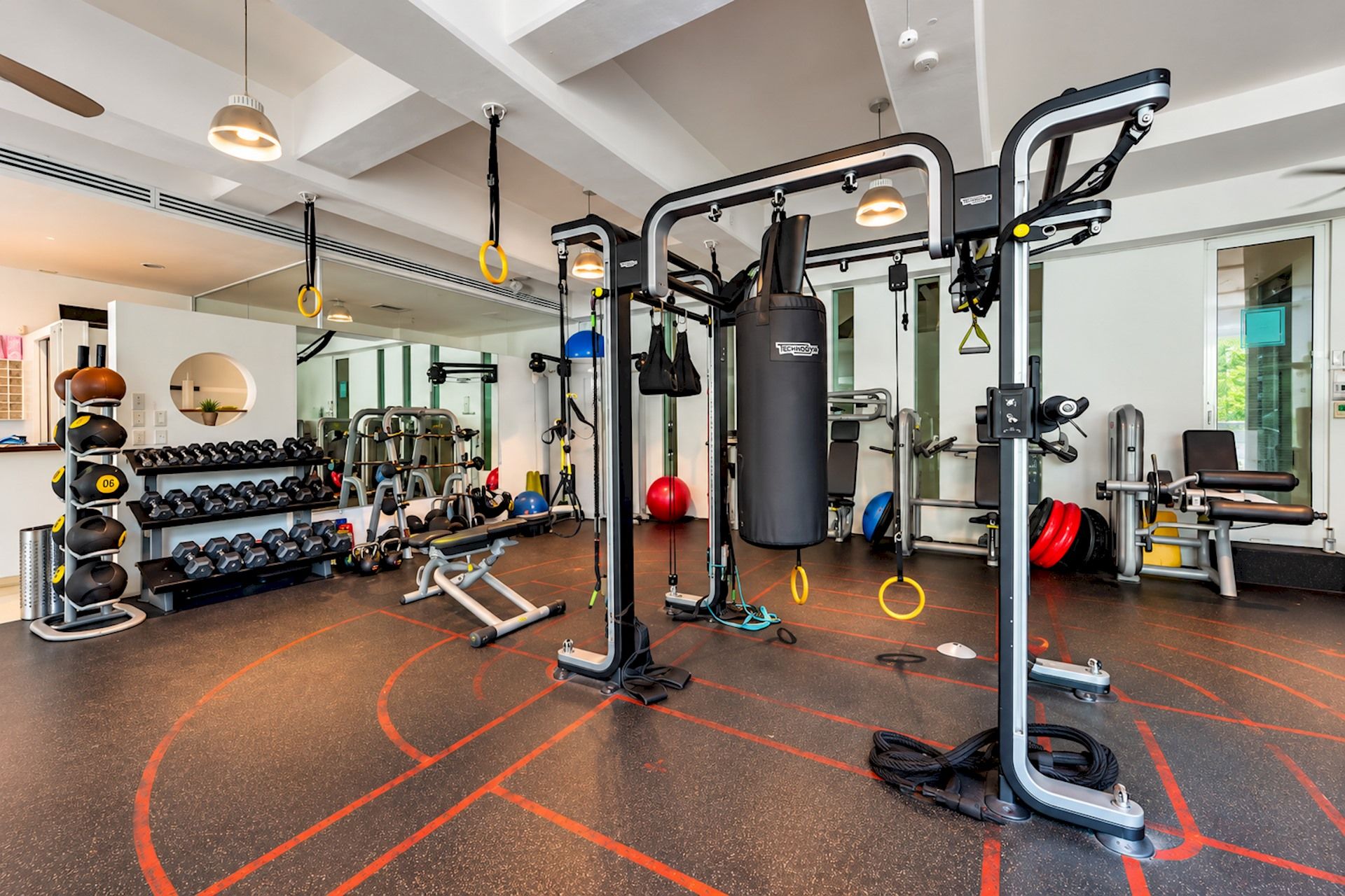 Une salle de sport équipée de divers appareils d’exercice, dotée d’un mur avec des miroirs et d’un sac de frappe fixé au mur.