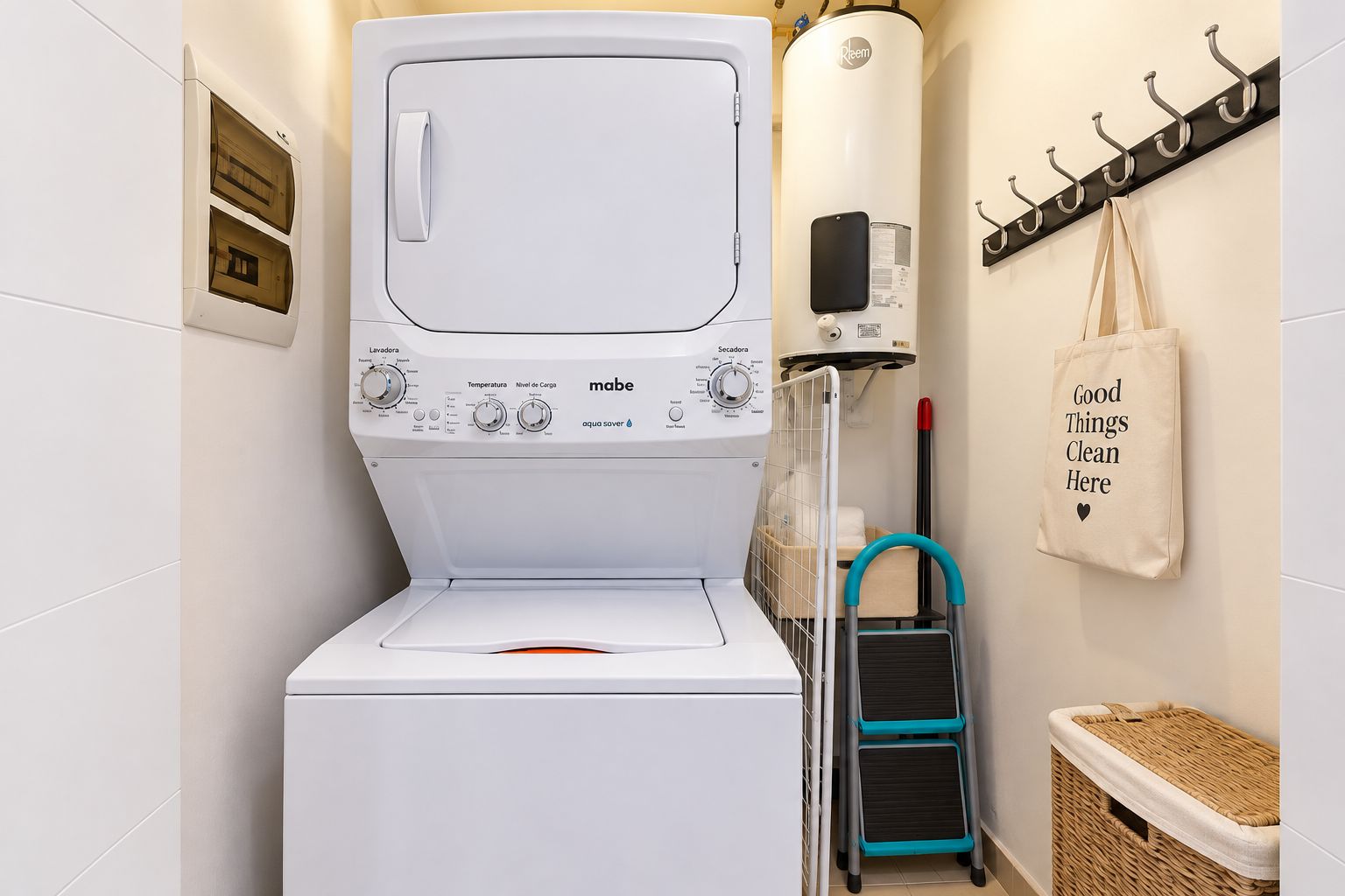 A compact laundry area with a front-loading mabe washer and dryer, a wall-mounted water heater, and a small step stool.