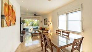 A spacious dining area with a large table and chairs, a ceiling fan, and a view of the outdoors through large windows. - Downtown Playa close 5th Av Rooftop Pool (Playa del Carmen)