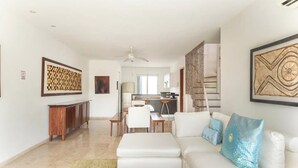 A modern living room with a white sofa, a dining area, and a kitchen in the background.