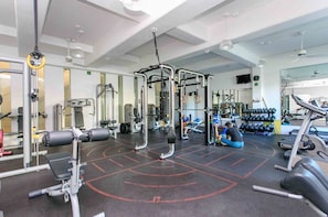 Et fitnesscenter med forskellig træningsudstyr, herunder vægtmaskiner, en squat-stativ og håndvægte.