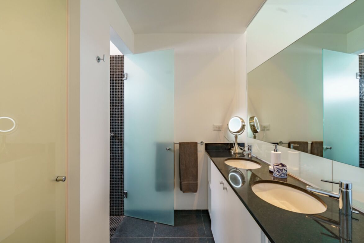 A modern bathroom with two sinks, a large mirror, and a glass shower enclosure.