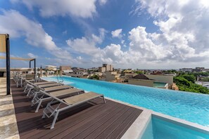 Ein Rooftop-Endlospool mit Liegestühlen, einer Holzterrasse und Blick auf die Stadt.