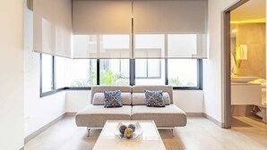 Un salon moderne avec un canapé, une table basse et de grandes fenêtres équipées de stores.
