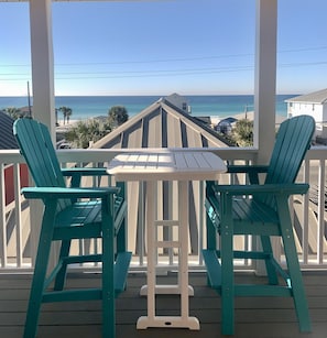A balcony with two green Adirondack chairs and a small white table, overlooking a beach and ocean. - ☀️ Steps from the beach, shops, breathtaking views of the Gulf and private pool 🌴 (Panama City Beach)