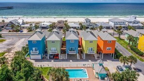 Une rangée de maisons colorées, avec une piscine au premier plan, une plage et une jetée en arrière-plan.