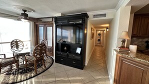 A spacious living area with a dining table, chairs, a black entertainment unit, and a kitchen with wooden cabinets. - Shoreline Towers 2076 (sleeps 7) Beach Setup Included (March 1-October 31) (Destin)