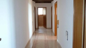 Um corredor com vigas de madeira, piso ladrilhado e uma porta no final.