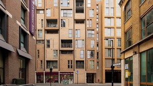 A multi-story building with a brick facade, multiple balconies, and a sign indicating 'Open every day 7am - 11pm'. - One Bed Apartment in Waterloo near Southwark (London)