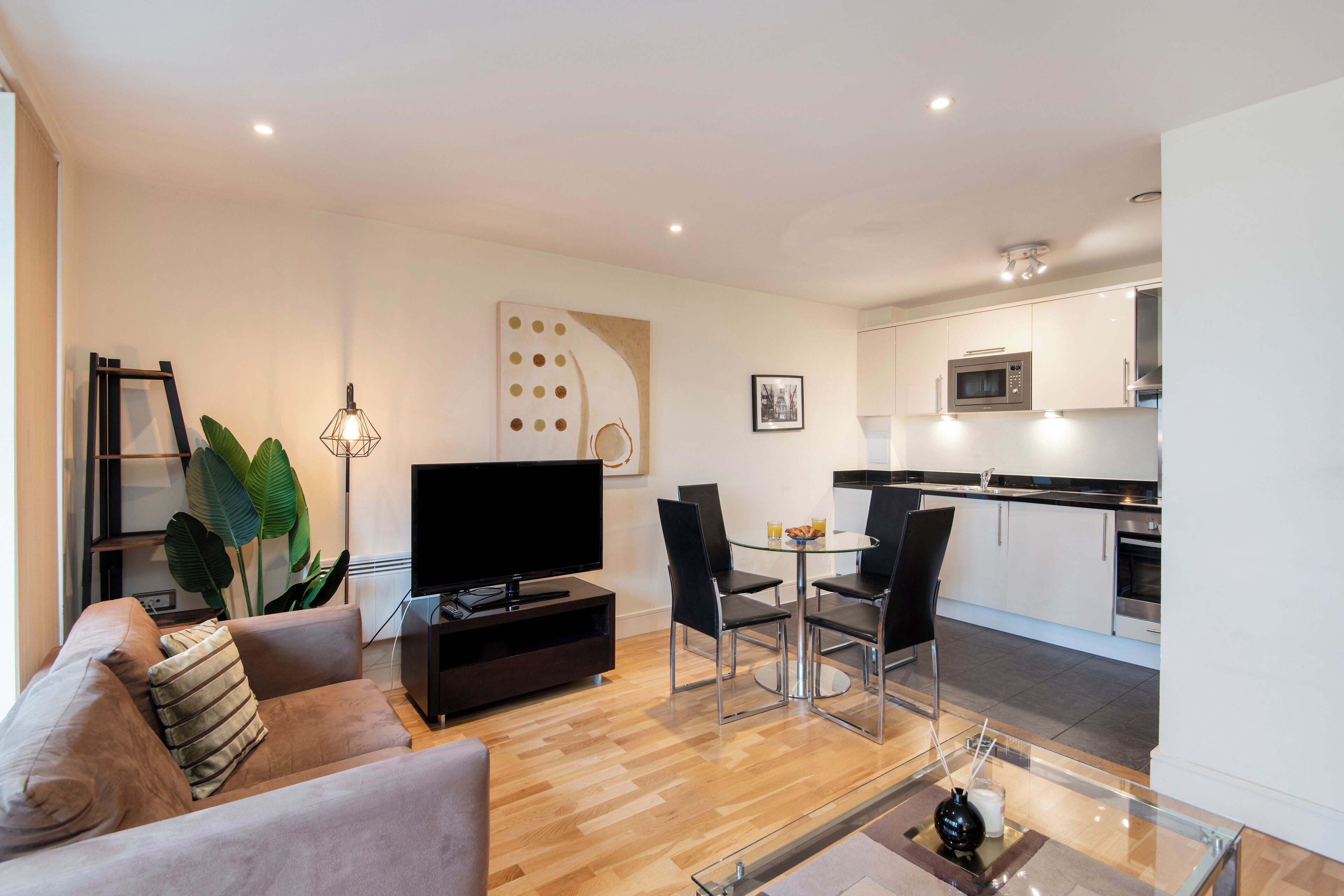 A modern living room with a flat-screen TV, a sofa, and a dining area with chairs and a glass table.