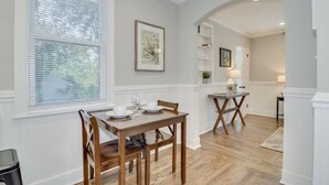 A dining area with a wooden table and chairs, a window with blinds, and a kitchen area in the background. - Cozy 2bd in Augusta - The Blue Bungalow (Augusta)