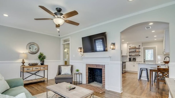 A spacious living room with a fireplace, a ceiling fan, and a kitchen in the background. - Cozy 2bd in Augusta - The Blue Bungalow (Augusta)