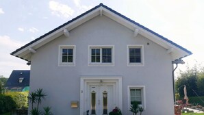 A two-story house with a white exterior, a front door with a glass panel, and three windows. There are potted plants in front of the house. - Haus Alexandra (Schwarzenbach an der Saale)