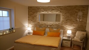 A bedroom with a bed, two bedside tables, a chair, a wall-mounted mirror, and a window with blinds. - Haus Alexandra (Schwarzenbach an der Saale)