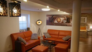A modern living room with orange furniture, a floor lamp, and a large abstract painting on the wall. - Haus Alexandra (Schwarzenbach an der Saale)