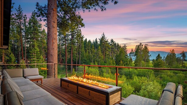 A deck with a built-in fire feature, outdoor seating, and a view of a forested landscape.