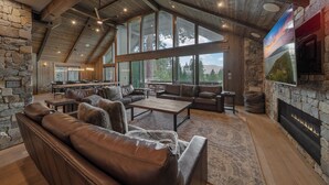 A spacious living room with leather sofas, a fireplace, stone walls, and large windows offering a view of the outdoors.