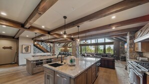 A spacious kitchen with a large island, wooden beams, stone accents, and a view to the outdoors.