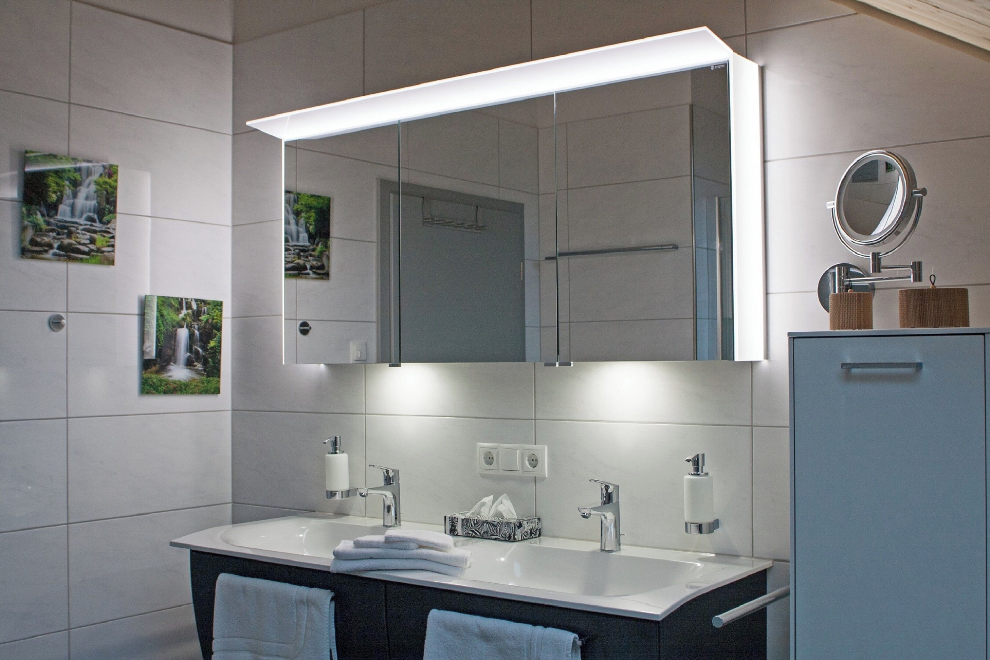 A modern bathroom with a large mirror, two sinks, and a cabinet.