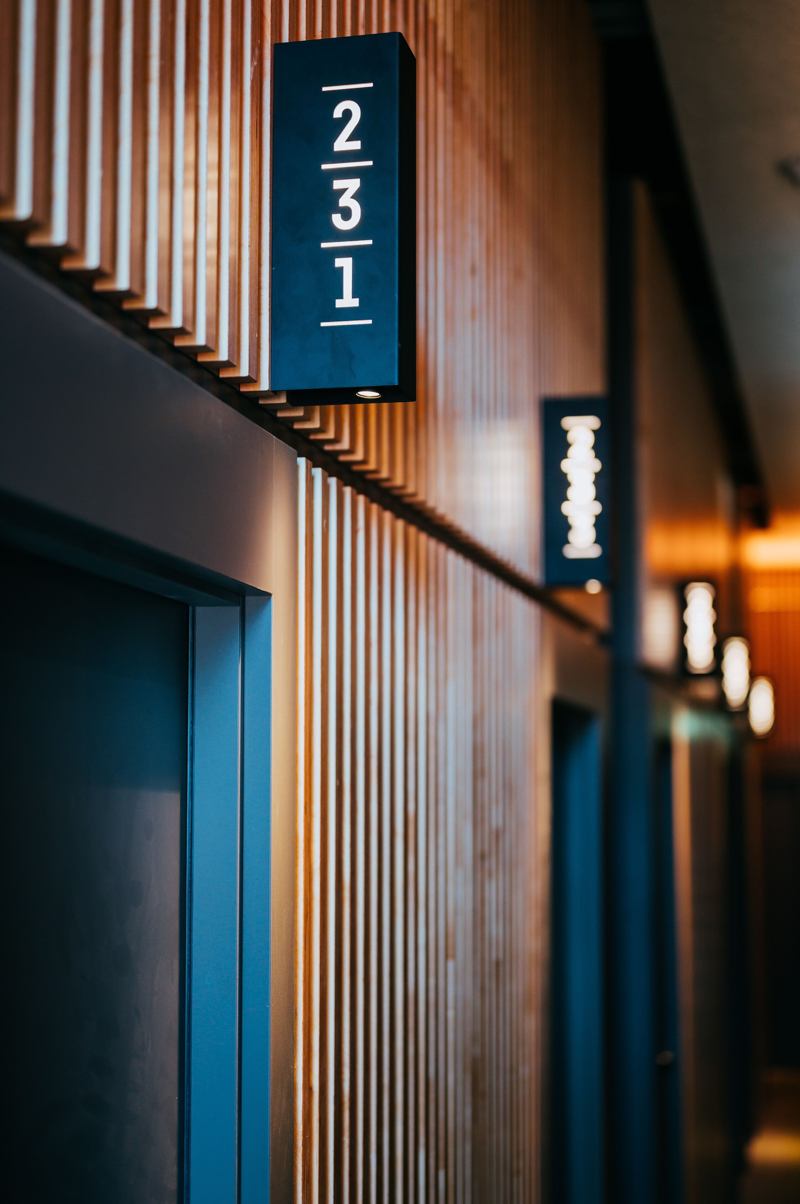 A hotel corridor with vertical wooden slats and a sign displaying room numbers.