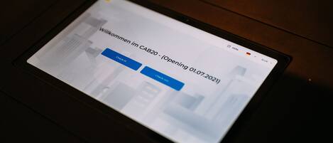A tablet displaying a webpage with the text "Willkommen im CAB20 - (Opening 01.07.2021)".