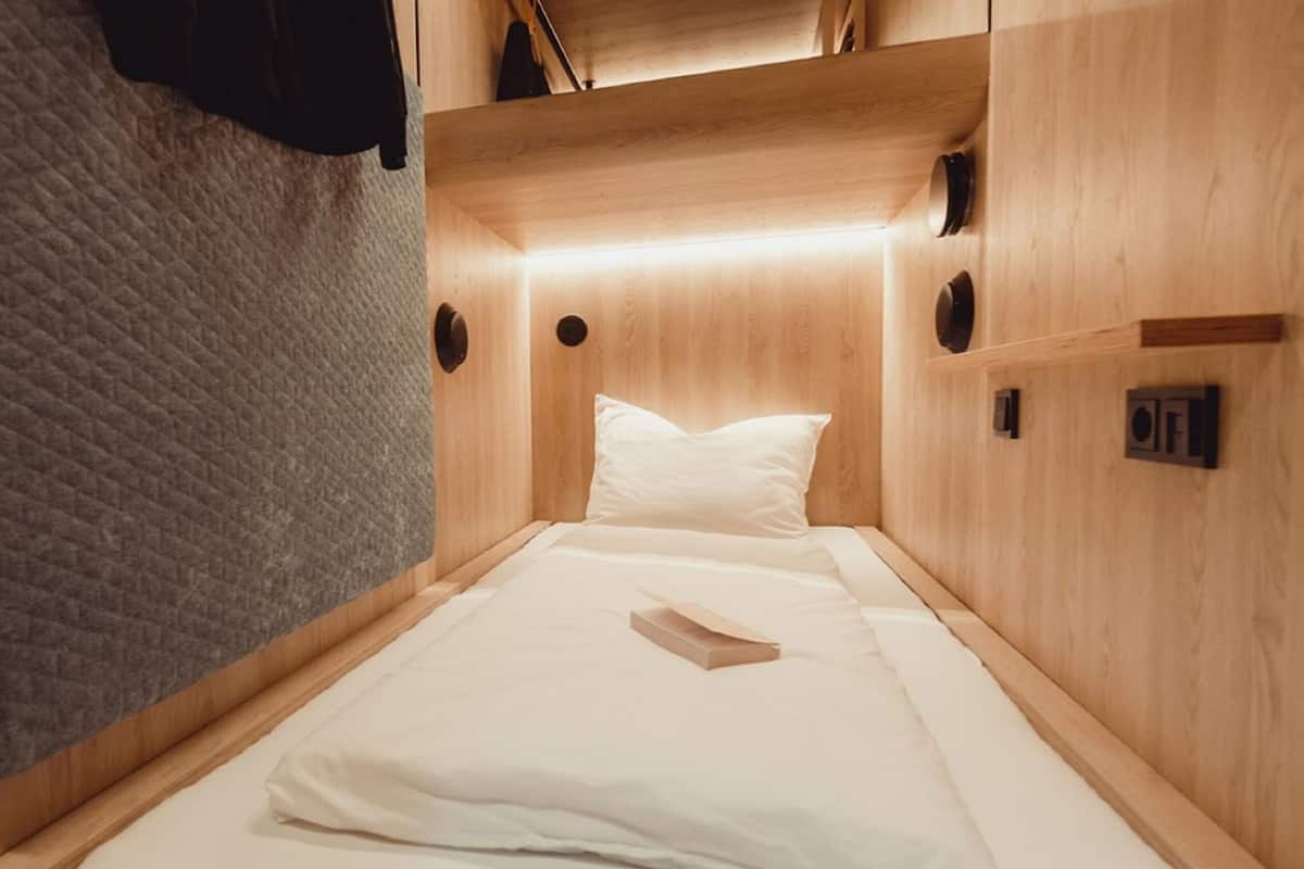 Una habitación compacta y bien iluminada con una cama, un edredón y un pequeño estante con objetos.