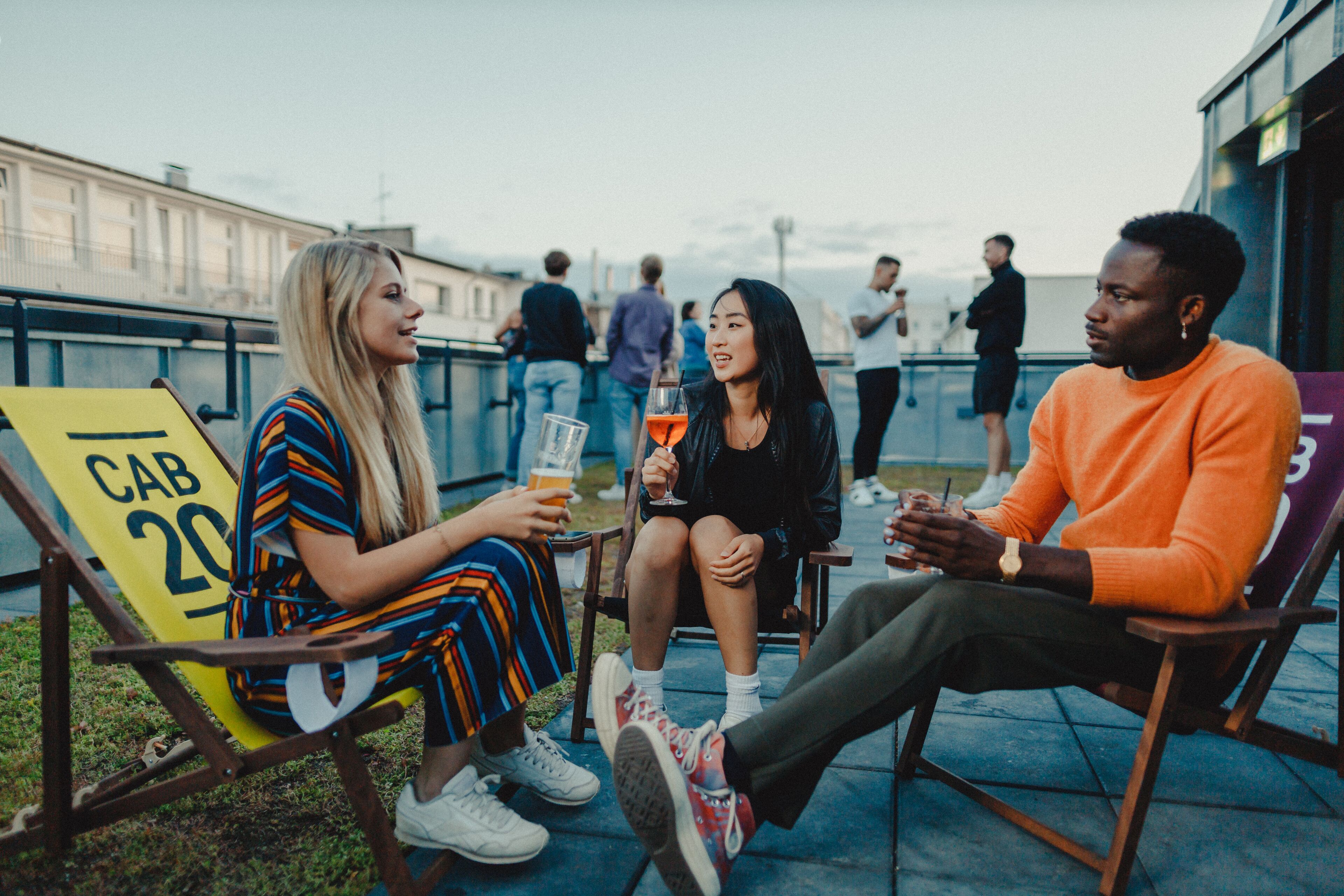 Three people seated on outdoor chairs with a cityscape in the background.