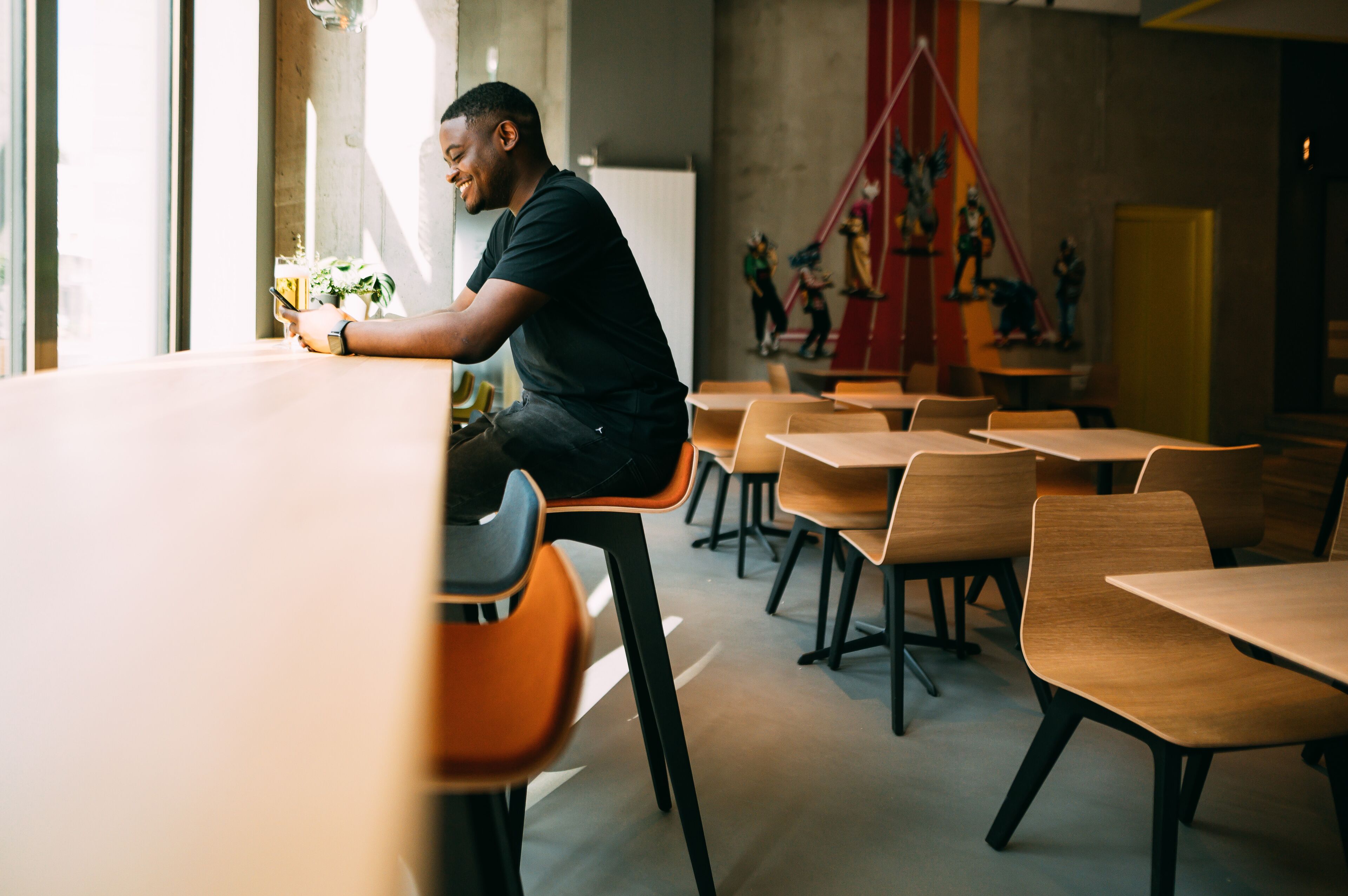 Un espace de restauration moderne avec des tables et des chaises en bois, une personne utilisant un smartphone et des œuvres d'art abstraites accrochées au mur.