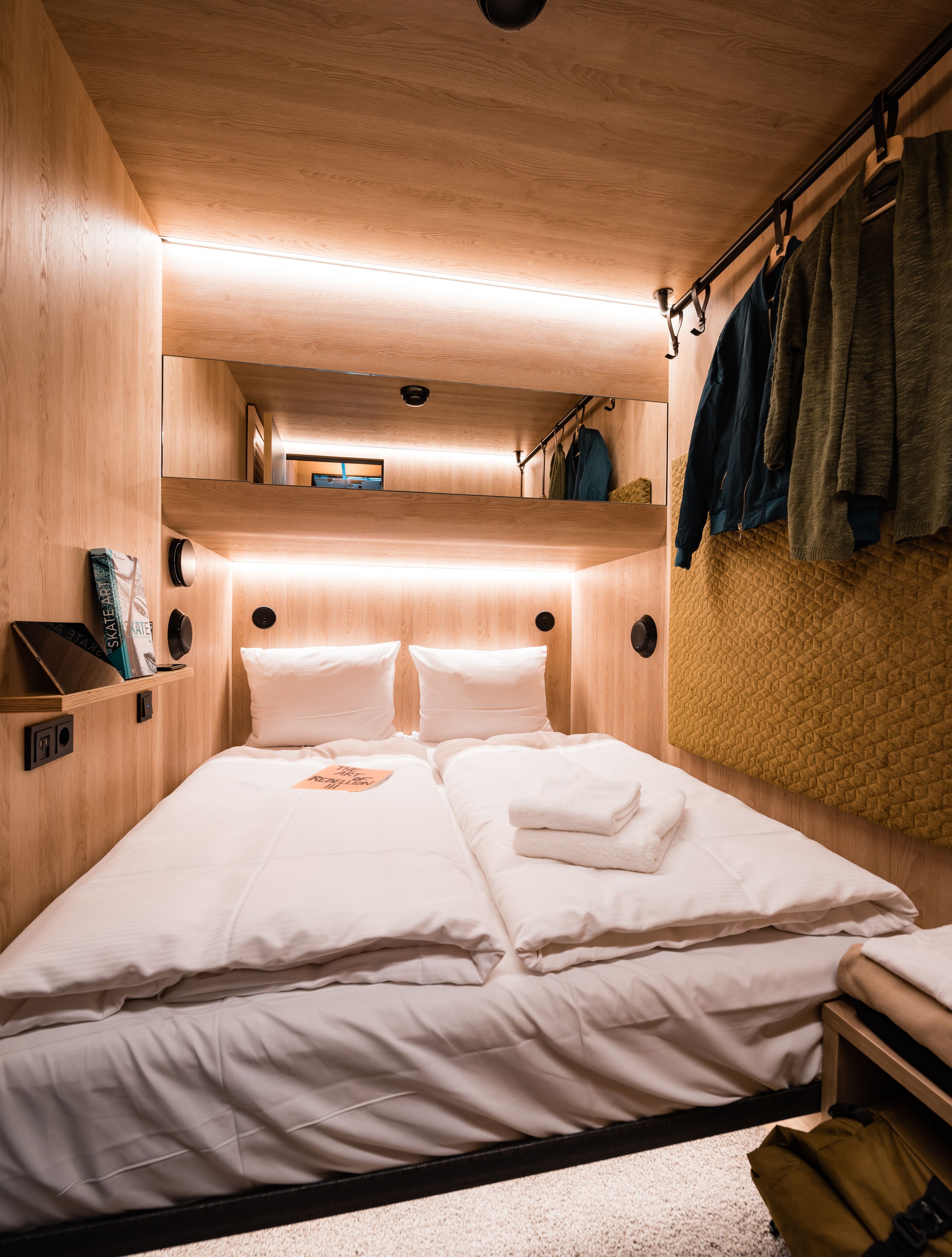 Una habitación pequeña y luminosa con una litera, una mesita de noche y un perchero.
