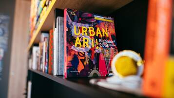 Une bibliothèque remplie de livres, dont un ouvrage intitulé « ART URBAIN ! Biennale 2019 » est mis en évidence.